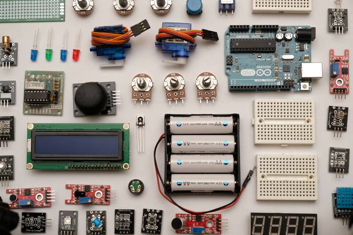 Arduino Uno microcontroller on a light grey surface surrounded by electonic components in a knolling pattern including joystick, LCD, batteries, servos, and sensors