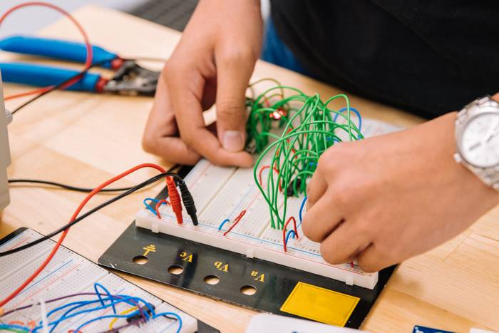 A males' hands pictured assembling a circuit on a breadboard with multiple green jumper wires.